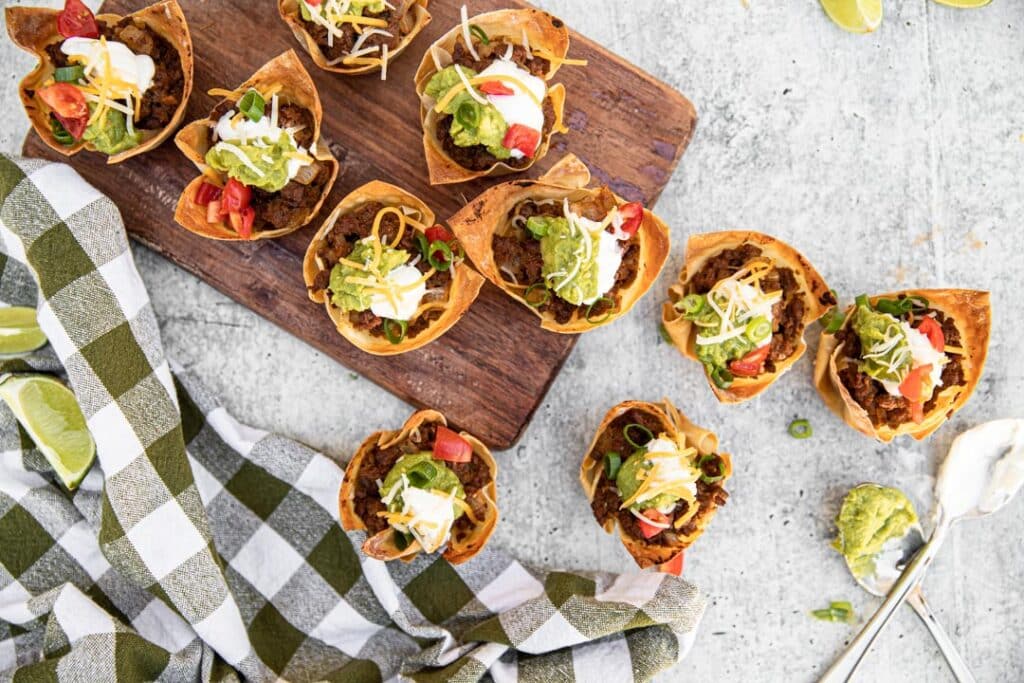 checkered towel, limes, guacamole, taco cups, taco meat, cutting board