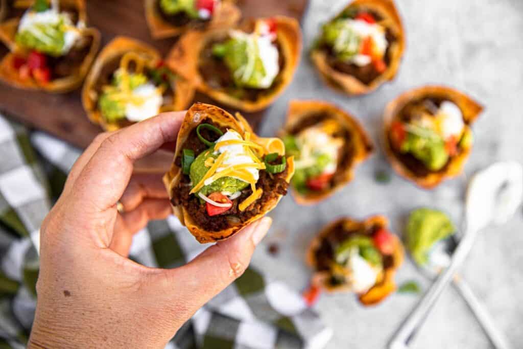 checkered towel, limes, guacamole, taco cups, muffin tin, taco meat, hand
