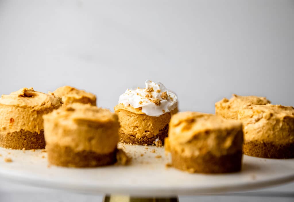 Mini pumpkin cheesecakes on a marble platter.  One has whipped cream and graham cracker crumb