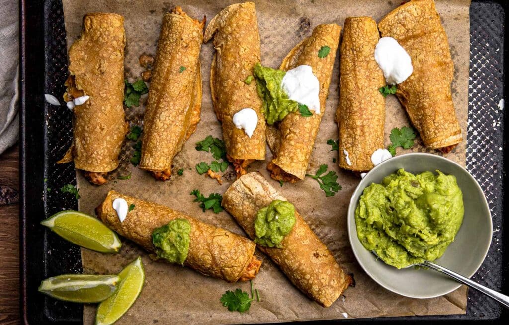 Crispy baked cream cheese taquitos on a baking sheet served with a side fo guacamole.