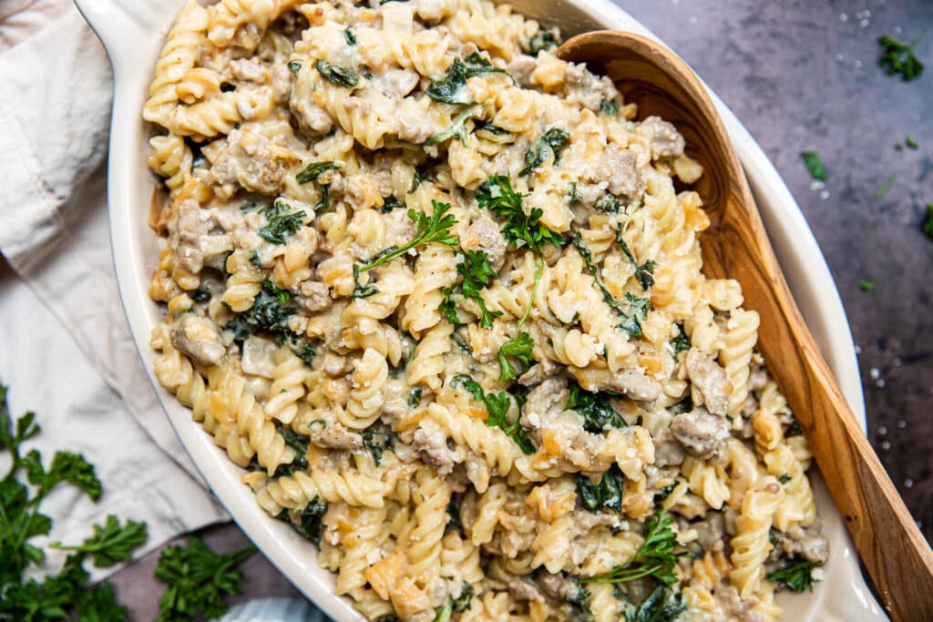 A big dish of creamy sausage and kale pasta.  A wooden serving spoon is on the side of the platter.