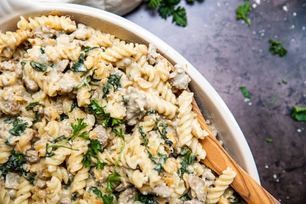 A big dish of creamy sausage and kale pasta.  A wooden serving spoon to the other side.