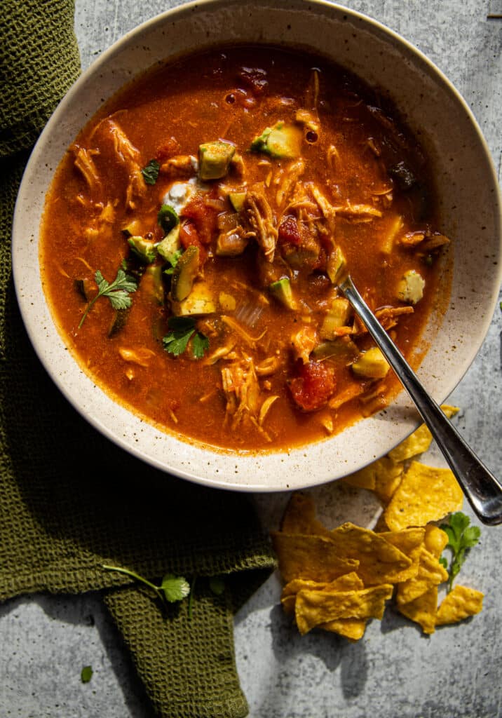 A bowl of chicken tortilla soup with a green linen to the side.  Chips below for serving